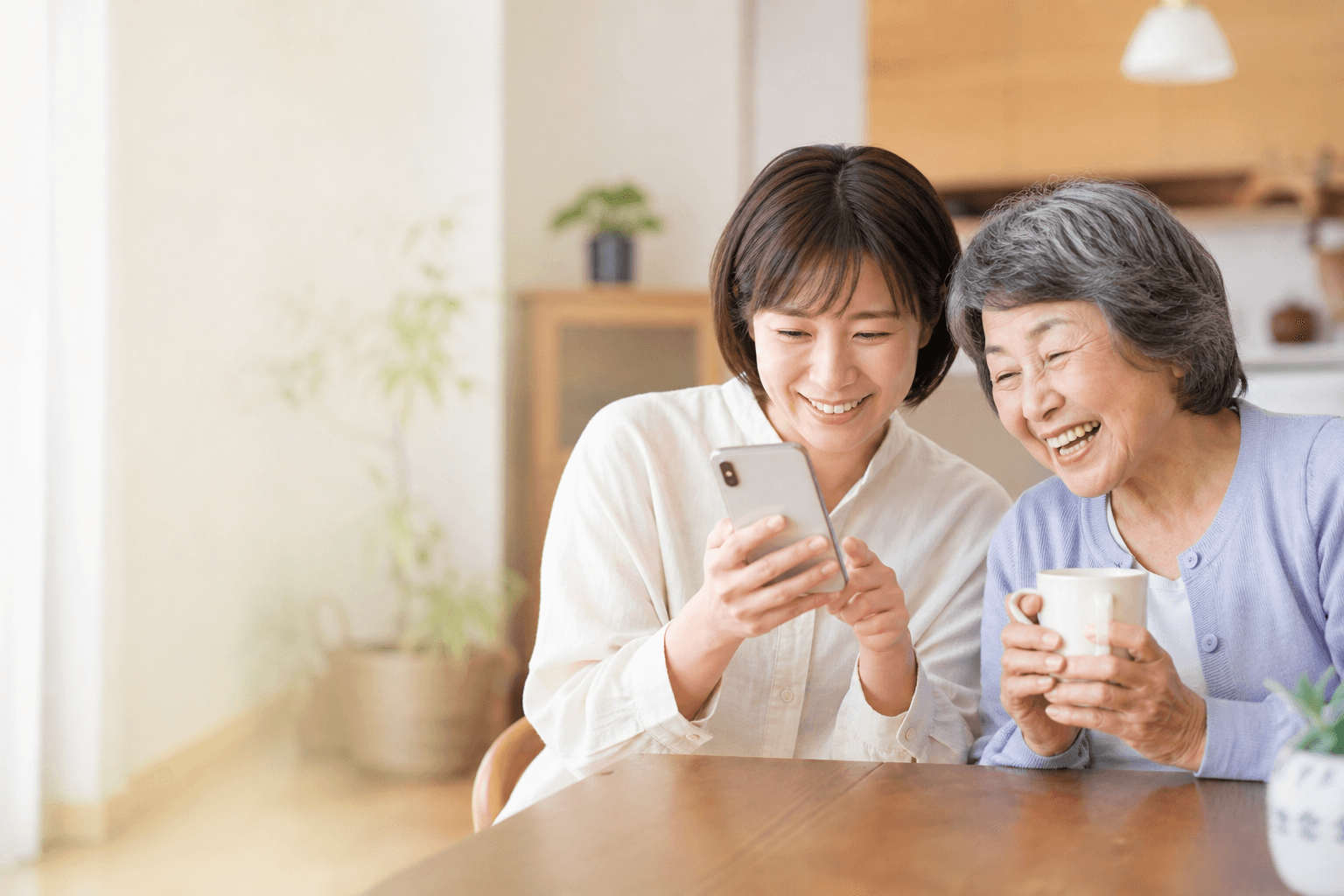 スマートフォンで見守りを確認する娘さんと、笑顔のおばあちゃん